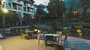 A wooden deck with outdoor seating and a hot tub, surrounded by greenery and a pond. - Ming Resort & Spa (Yuyao)