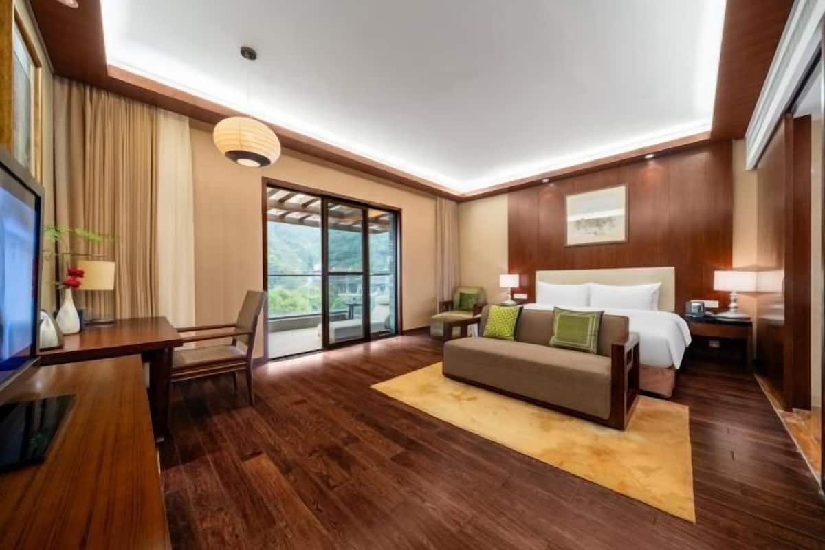 A hotel room with a wooden floor, a sofa, a bed, a desk, and a TV.