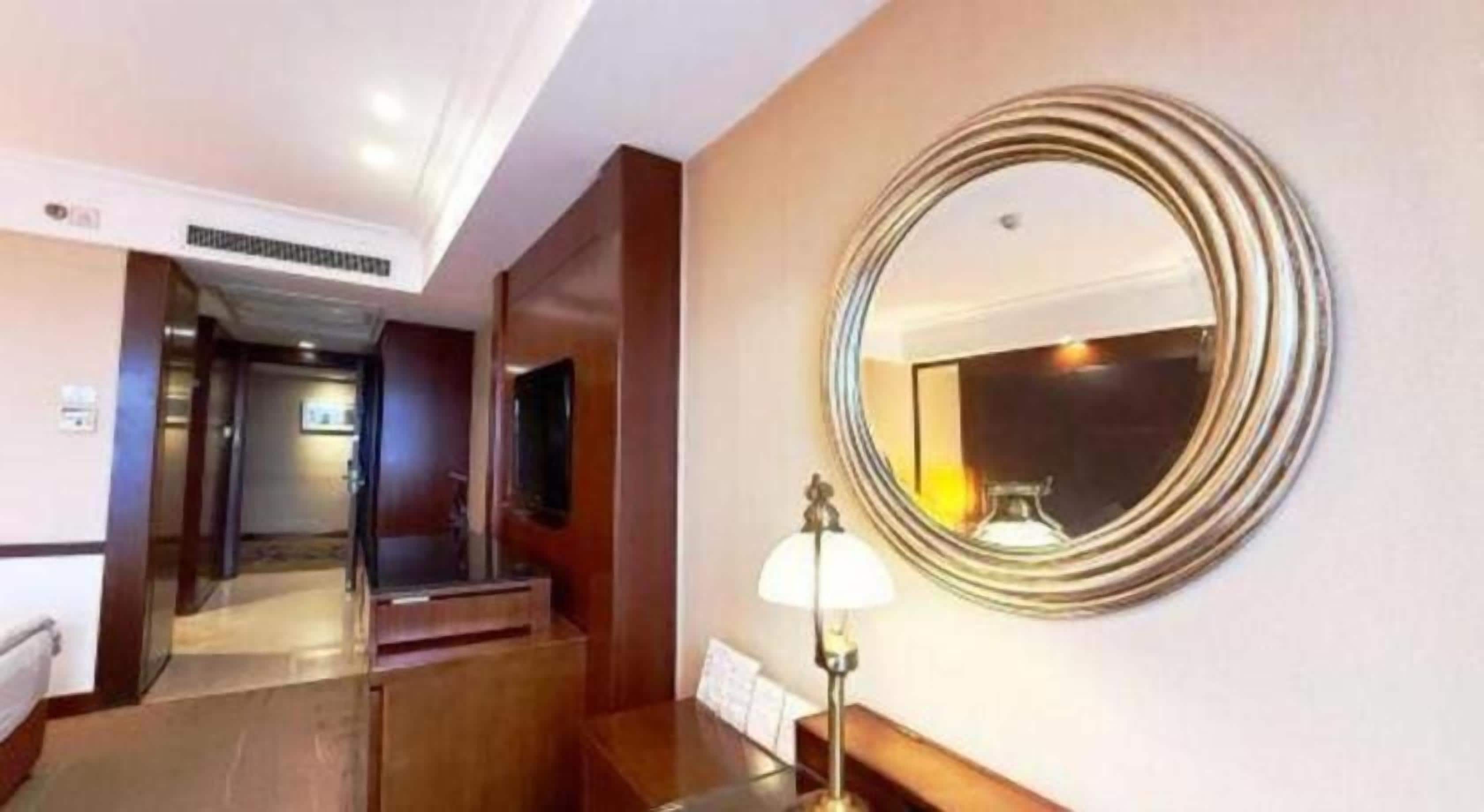 A hotel hallway with a round mirror, a lamp, and a reception desk.