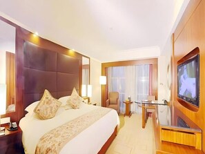 Quarto de hotel com uma cama grande, televisão, escrivaninha com cadeira e janela com cortinas.