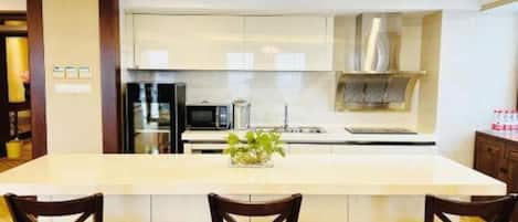 A modern kitchen with a central island, two bar stools, and a stainless steel range hood.