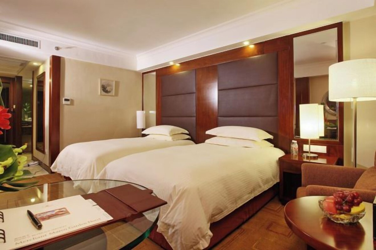 Ein Hotelzimmer mit zwei Betten, einem Glastisch, einem Stuhl, einer Lampe und einer Obstschale.