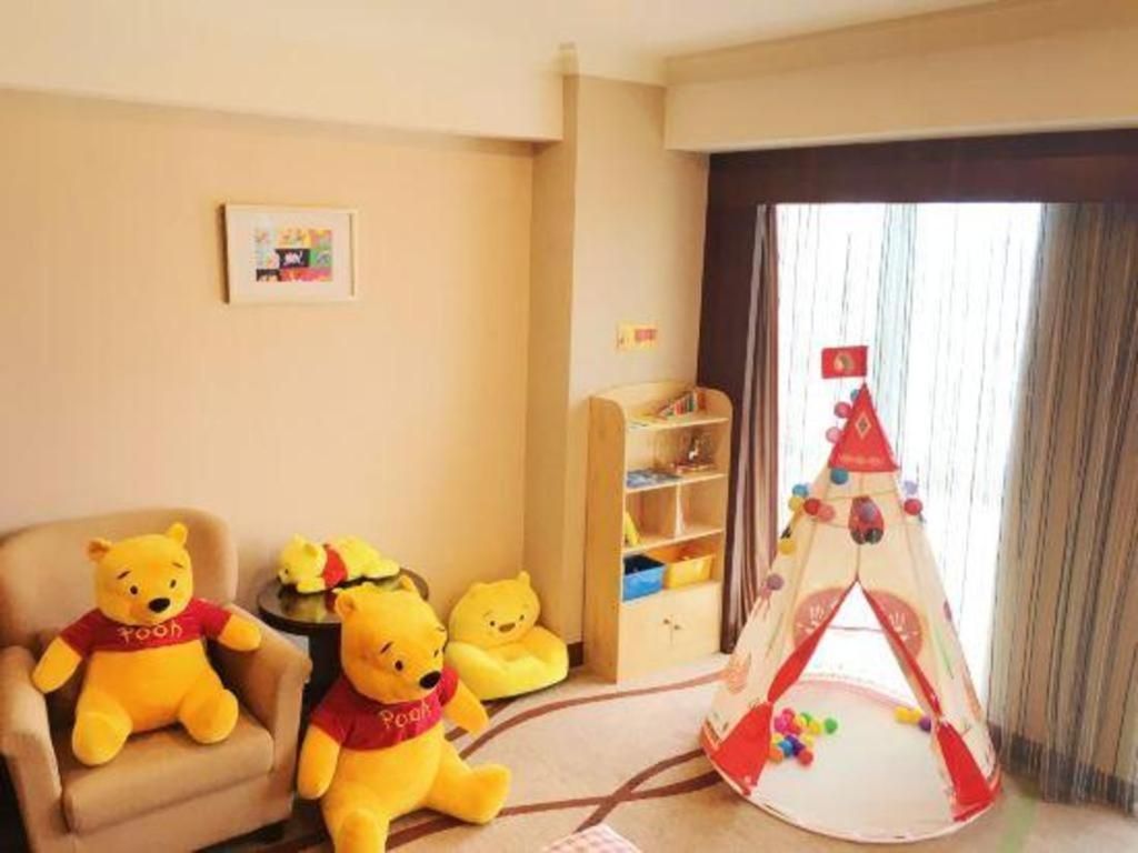 Quarto com poltrona bege, dois brinquedos macios, estante e uma tenda de brincar.