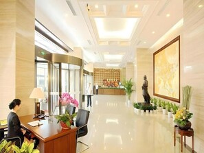 Un hall d’hôtel comprenant un comptoir d’accueil, un réceptionniste, un bureau de réception, un espace d’accueil, une statue et des plantes en pot.