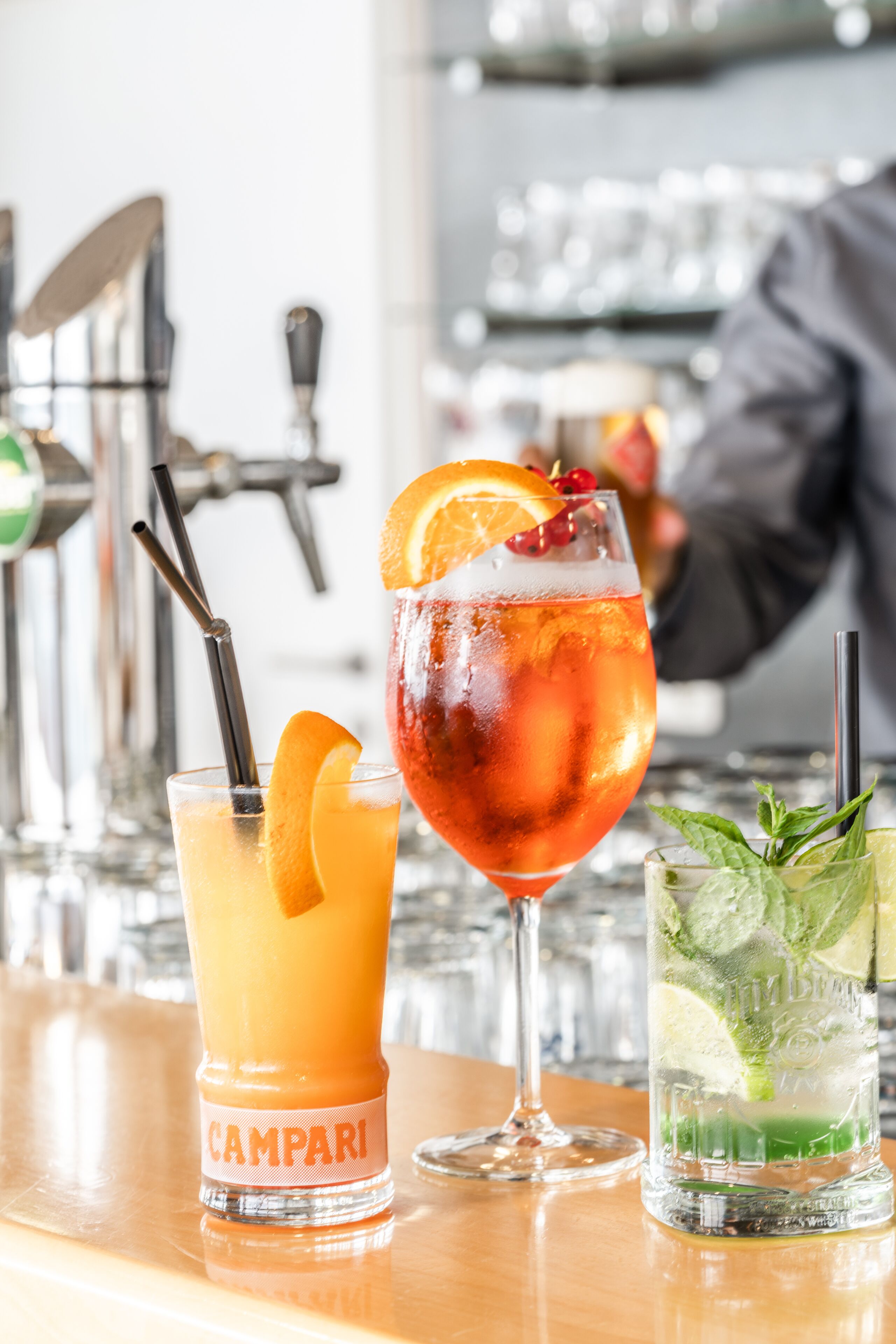 A bar with various drinks, including a Campari glass, a cocktail with an orange slice, and a mojito.