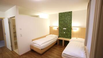 A hotel room with two single beds, a wooden bench, a green wall panel, and a mirror.