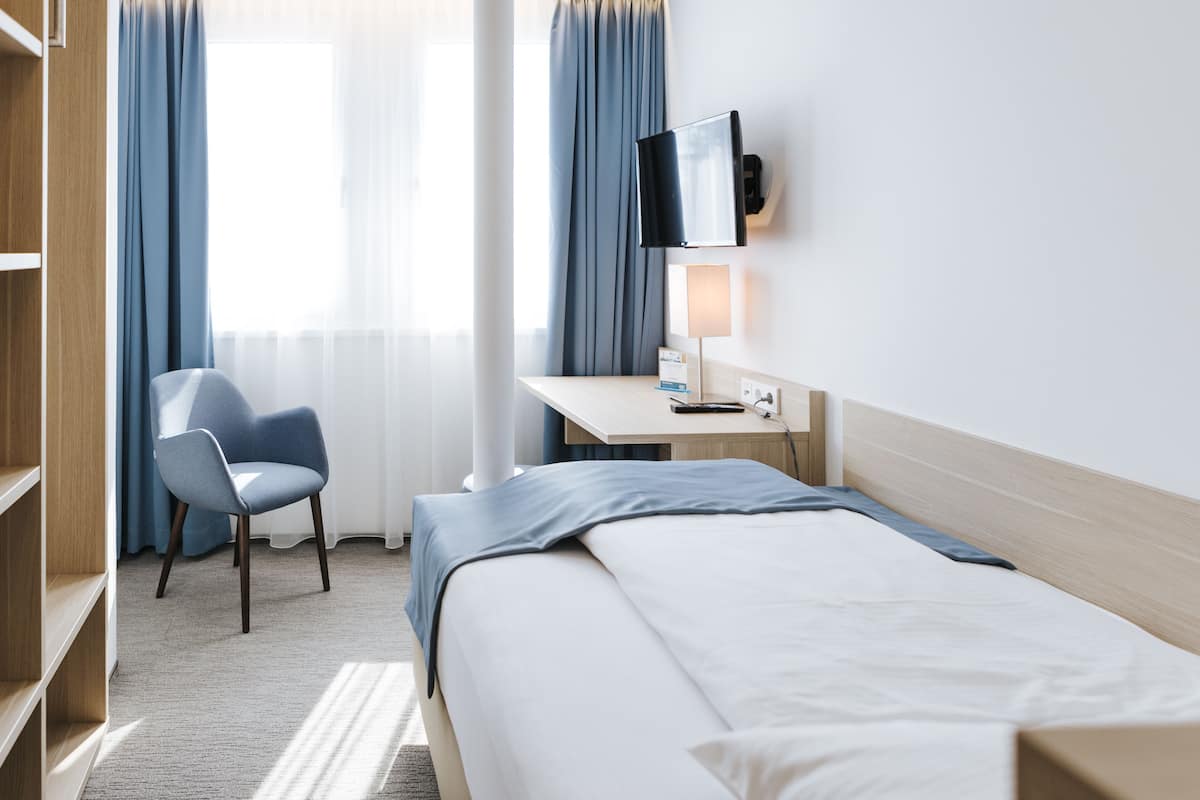 Habitación de hotel con cama, escritorio con televisor de pantalla plana, una silla y estantería.
