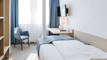 Habitación de hotel con cama, escritorio con televisor de pantalla plana, una silla y estantería.