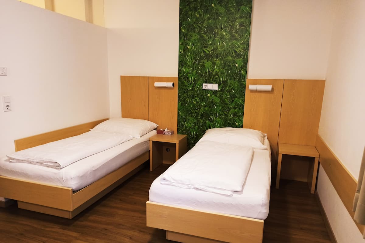 Dos camas individuales con cabeceros y mesitas de noche de madera, una pared verde con jardín vertical y suelo de madera.
