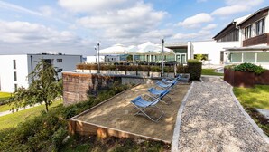 A rooftop lounge area with sun loungers, a gravel path, and a view of modern buildings and a clear sky. - Sankt Magdalena (Linz)