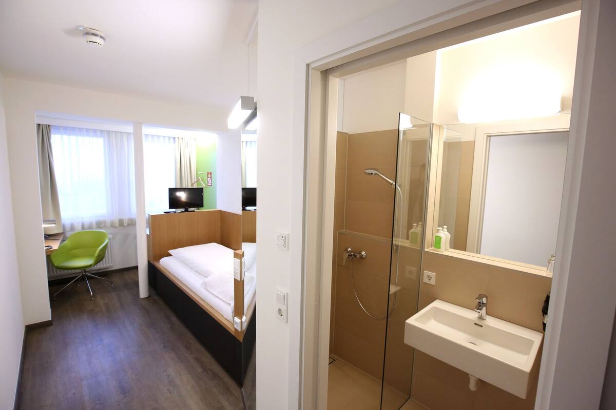 Una habitación de hotel con cama, escritorio, silla, ducha y lavamanos.