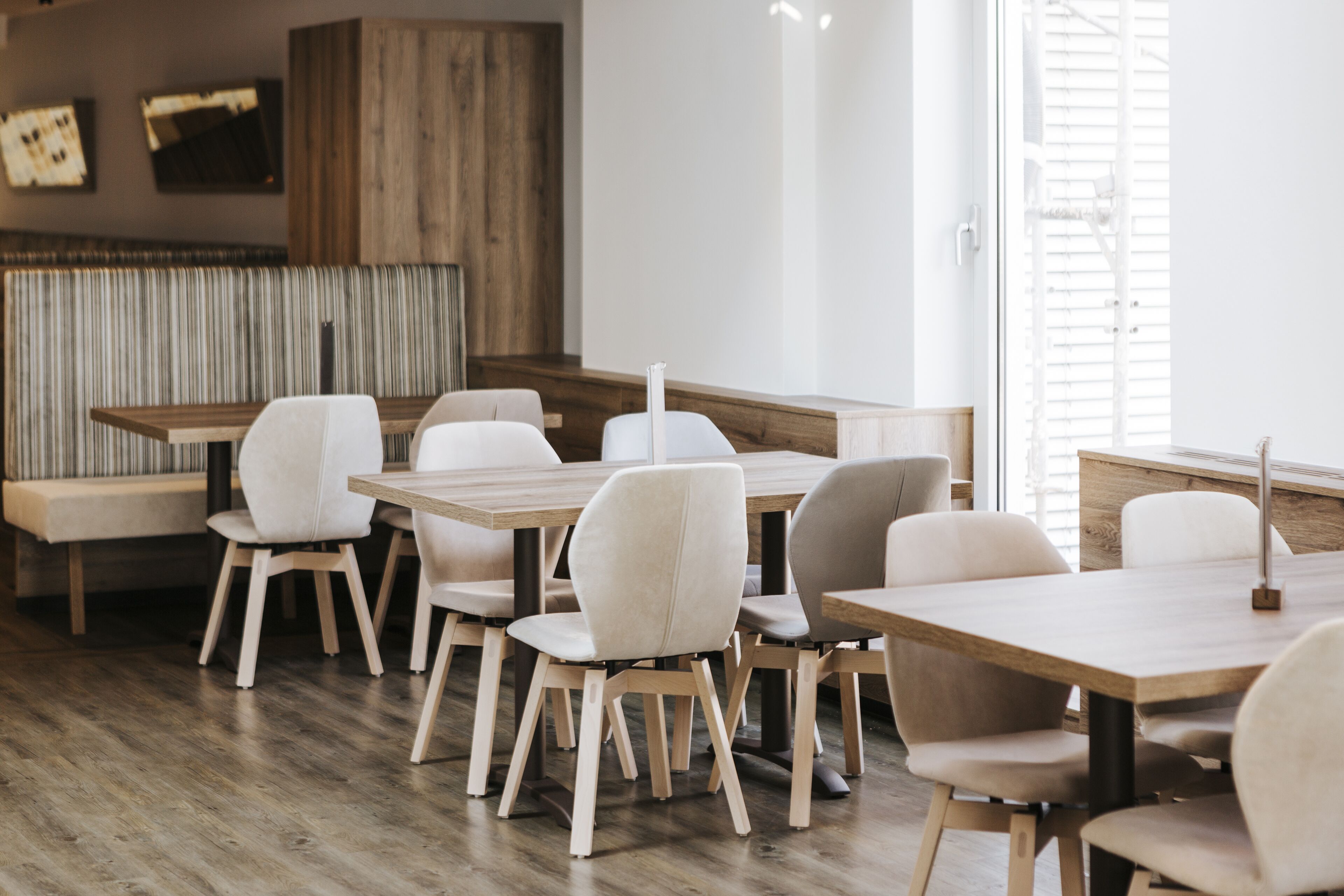 Uma sala de jantar moderna com mesas e cadeiras de madeira, um banco e uma parede de madeira com luminária.