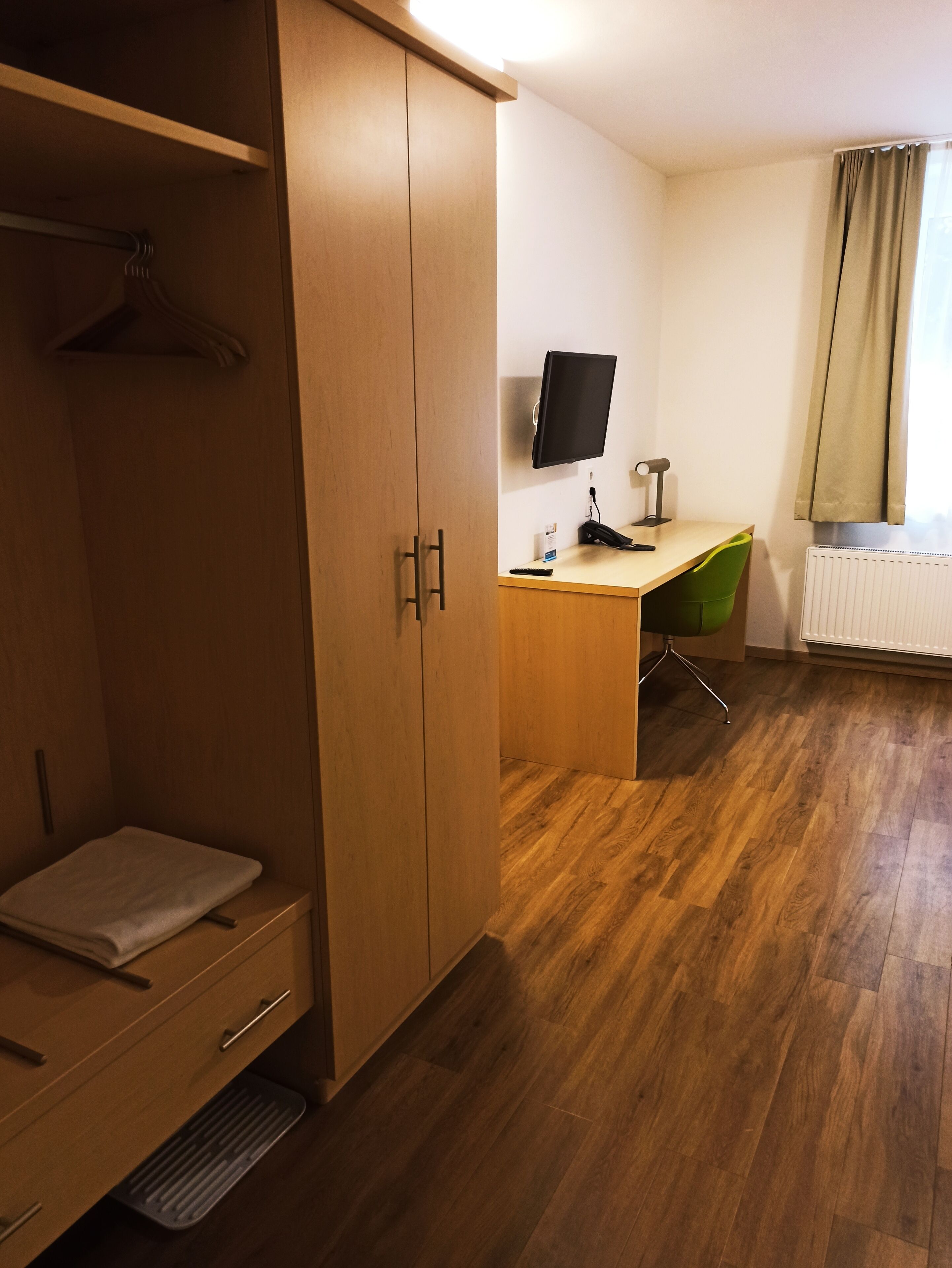 Una habitación con un armario de madera, un escritorio con una computadora y una silla, y un radiador.