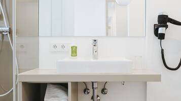 Un baño moderno con un lavabo blanco, un espejo, un secador de pelo y un cesto de basura.
