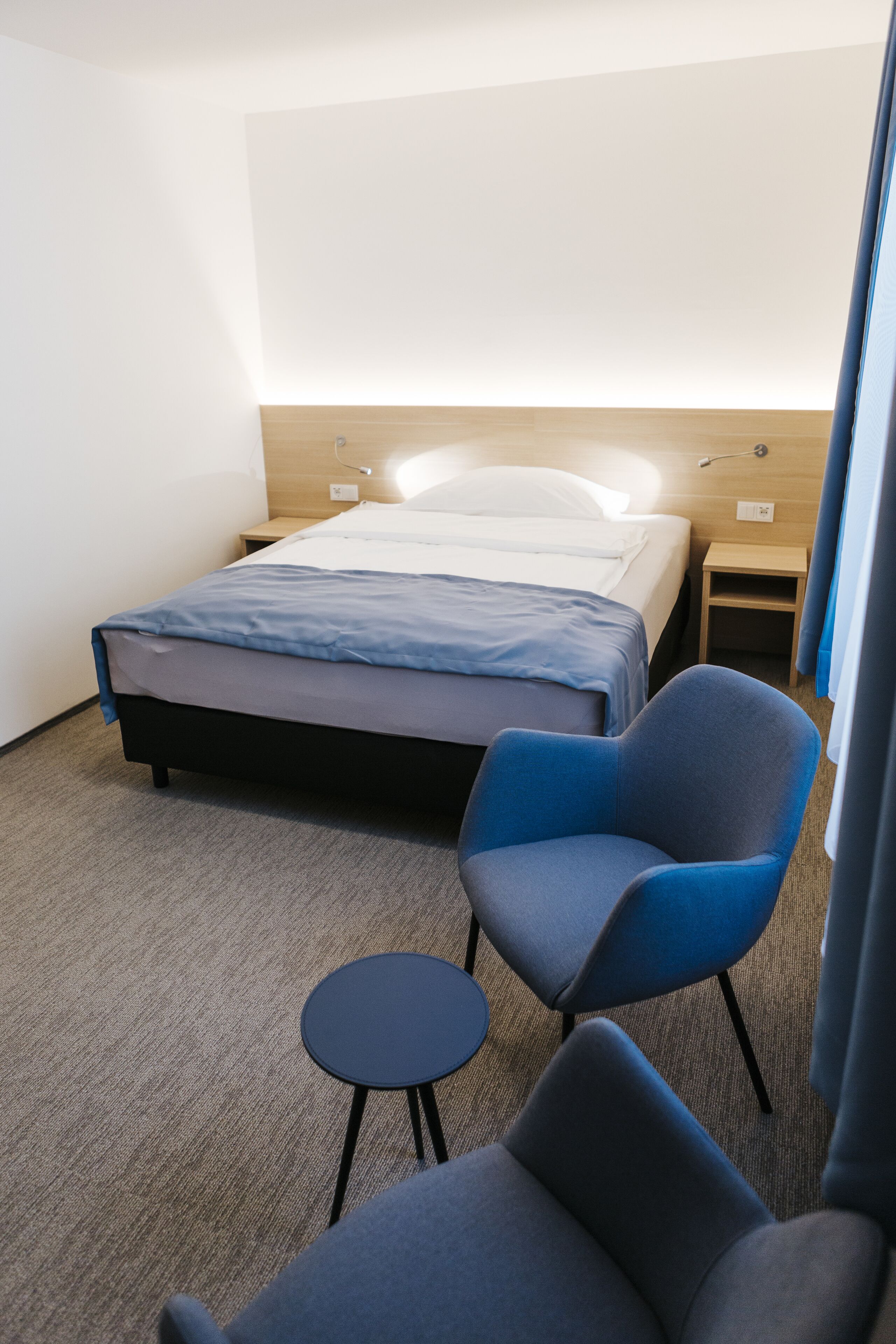Une chambre d’hôtel avec un lit, deux chaises, une petite table et une table de chevet.