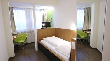 Una habitación de hotel con una cama individual, un escritorio con silla, un televisor y un radiador.