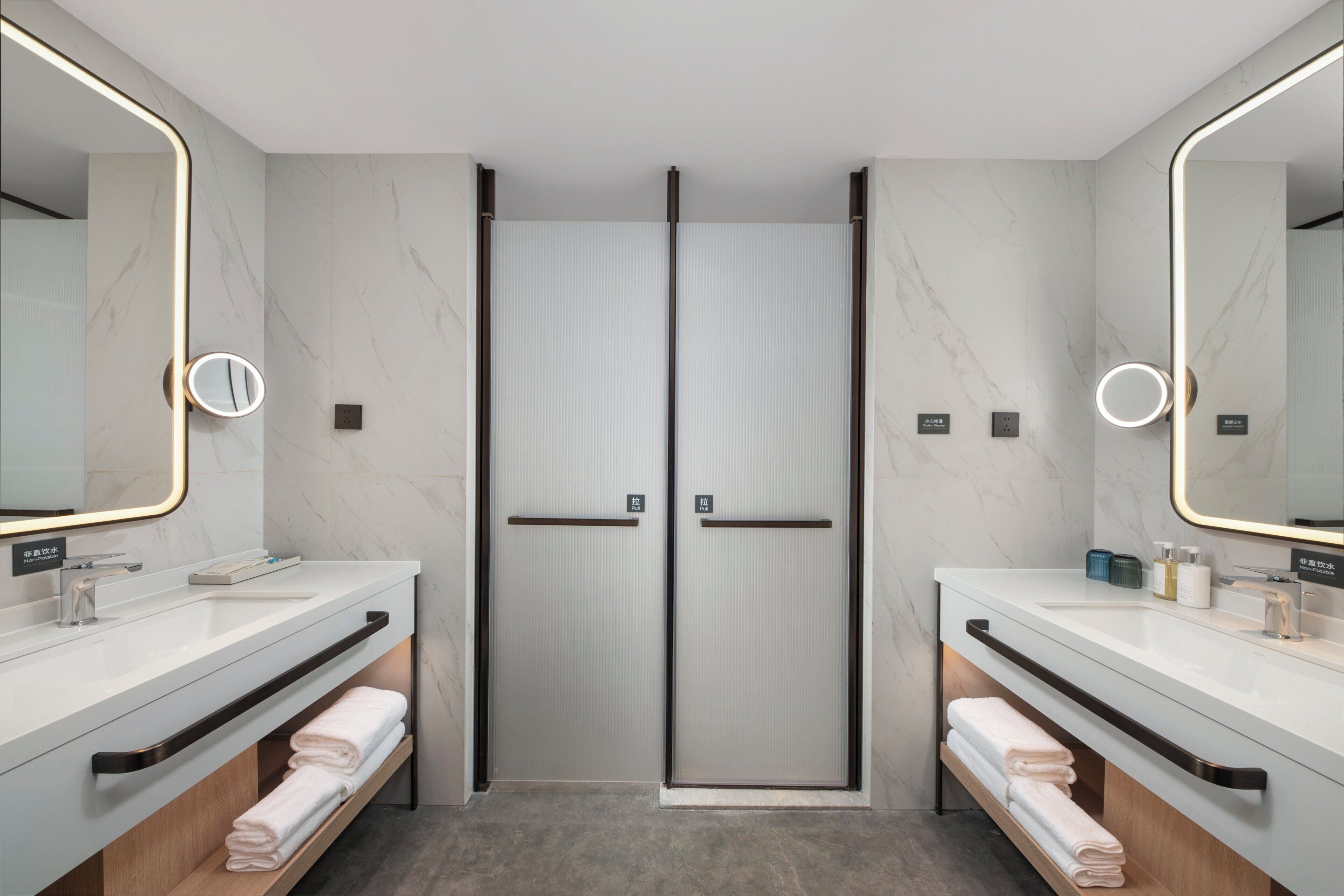 Un baño moderno con dos lavamanos, cabina de ducha de vidrio y un espejo grande.