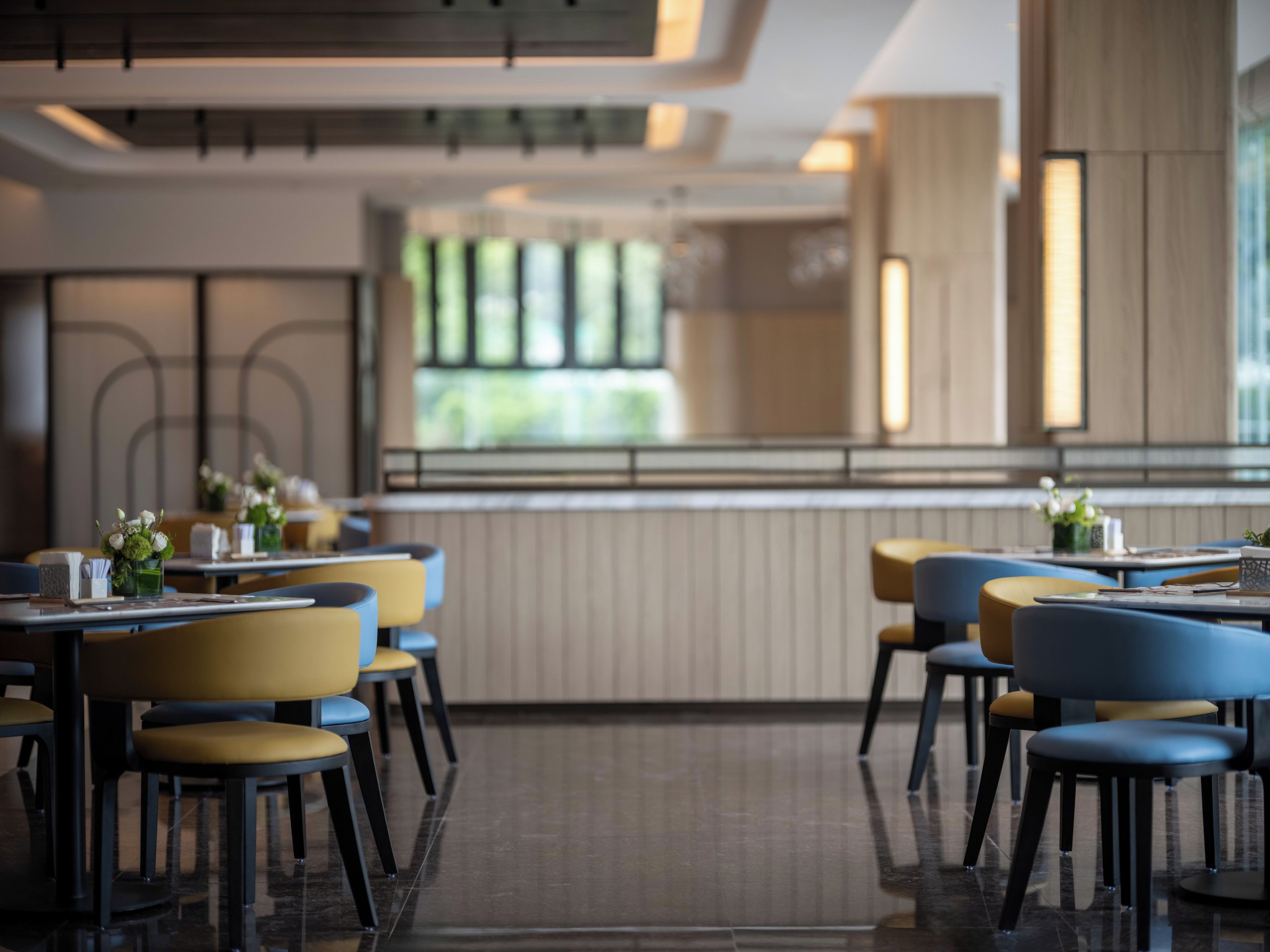 A modern restaurant interior with a long counter, multiple tables, and chairs.