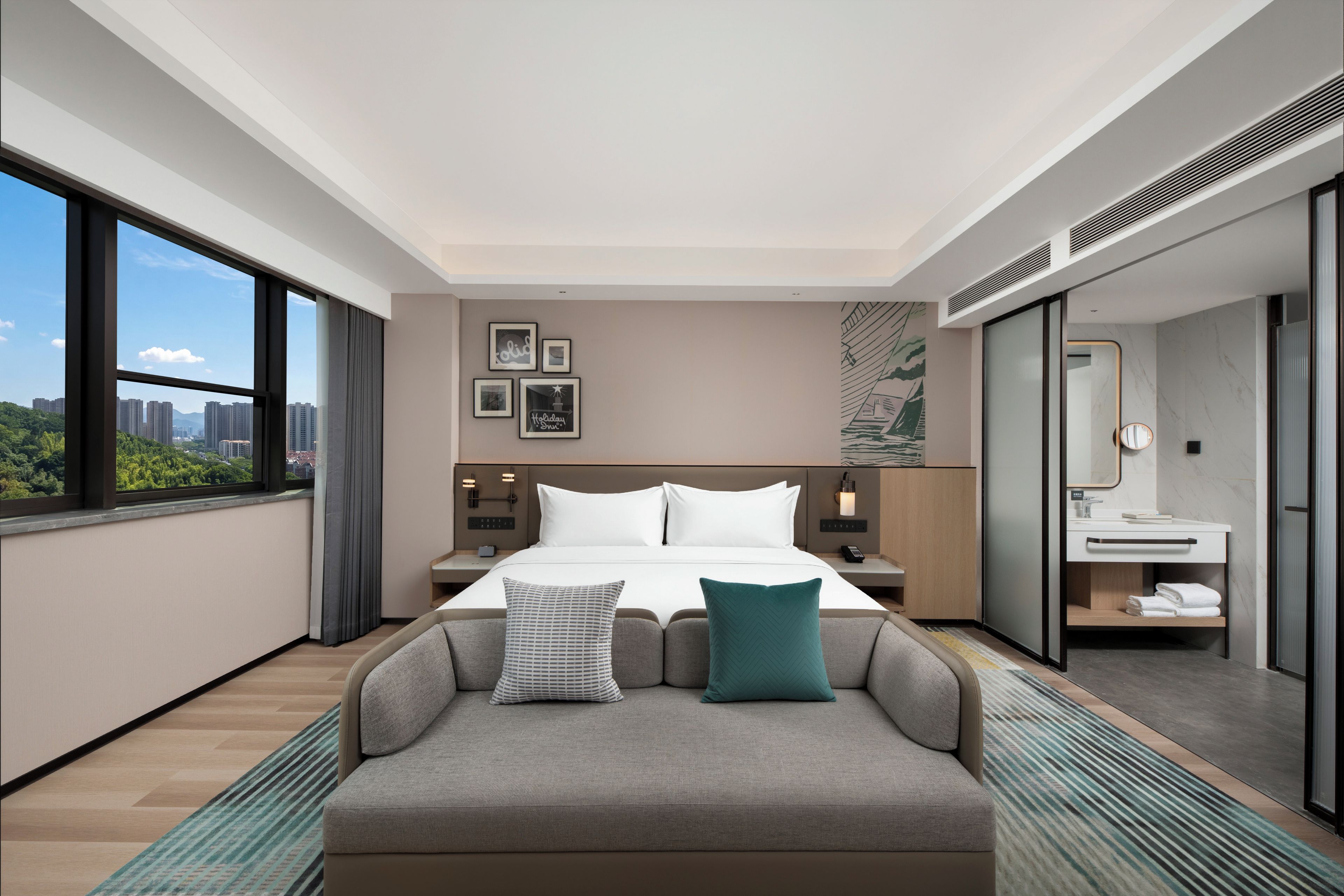 Habitación de hotel con cama, sofá, mesita de noche, baño y vistas a la ciudad.