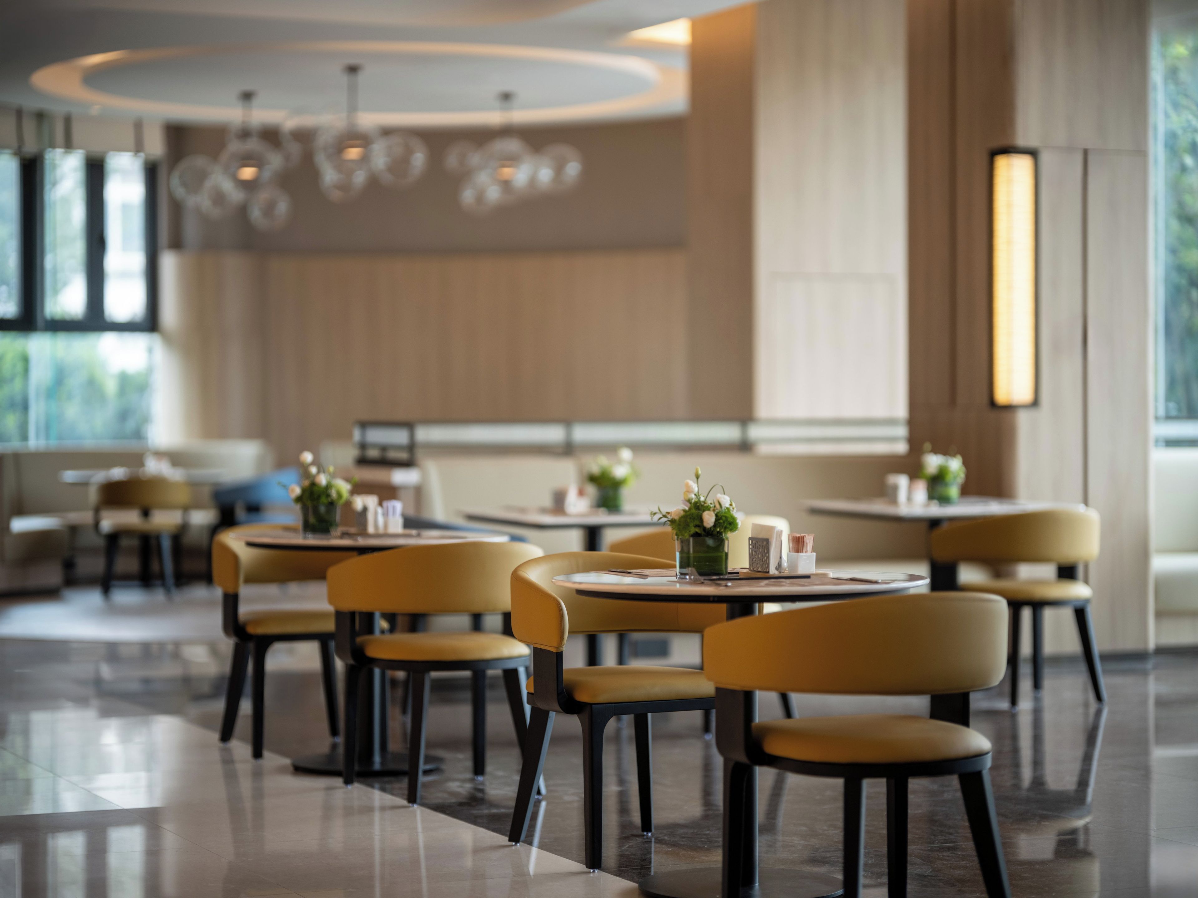 Un interno ristorante moderno con tavoli e sedie rotonde, illuminazione a sospensione e vista sull'esterno.