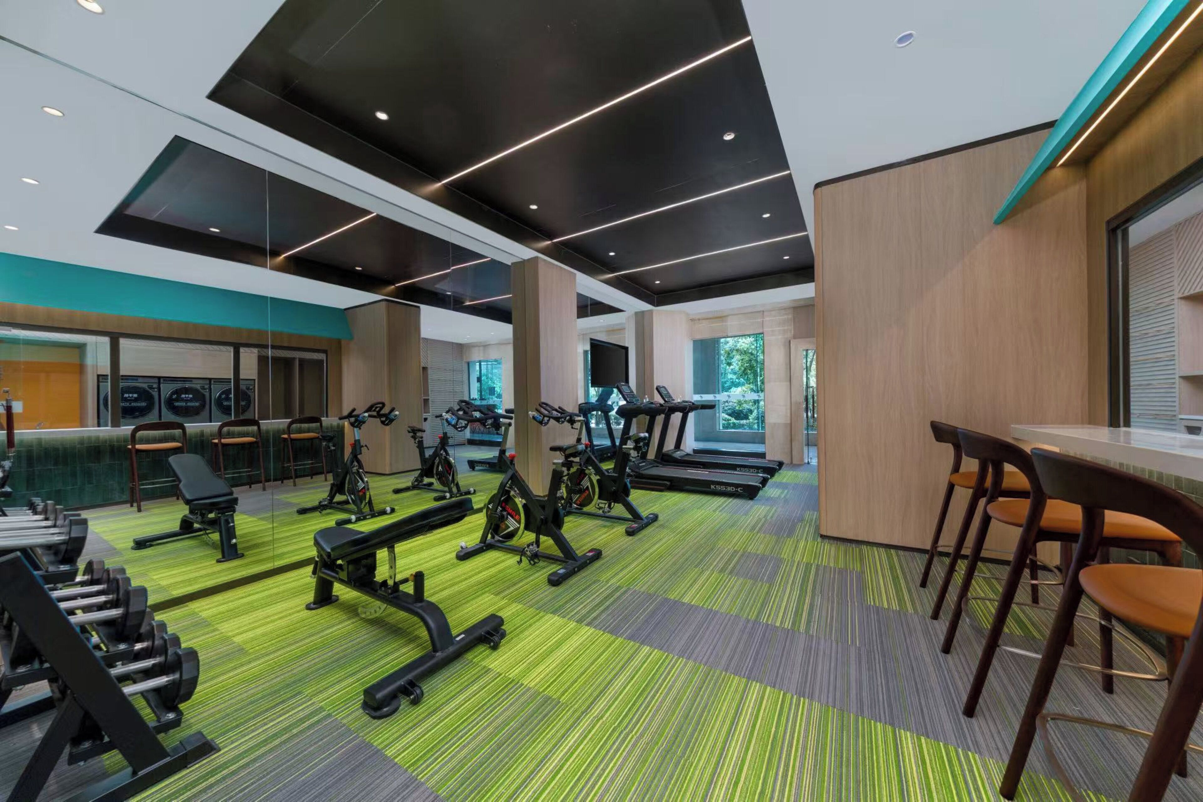 Un gimnasio con equipo de ejercicio, un espejo grande y una zona de estar con sillas.
