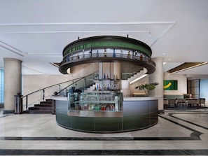 Zona de bar circular con cerramiento de vidrio, una escalera y un mostrador de recepción.