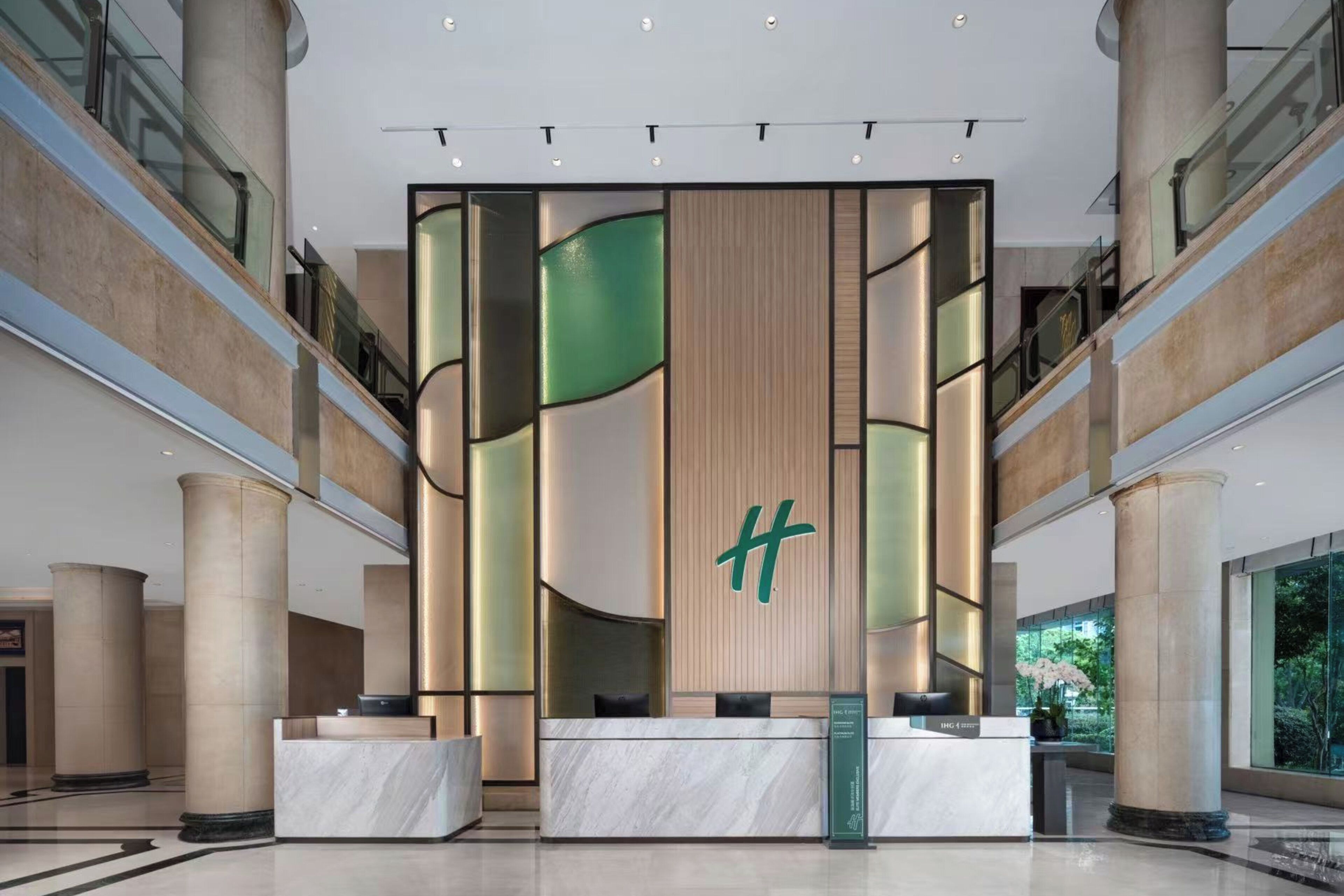 Un moderno vestíbulo de hotel con una recepción, grandes columnas y vistas al exterior.