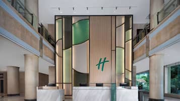 Un moderno vestíbulo de hotel con una recepción, grandes columnas y vistas al exterior.