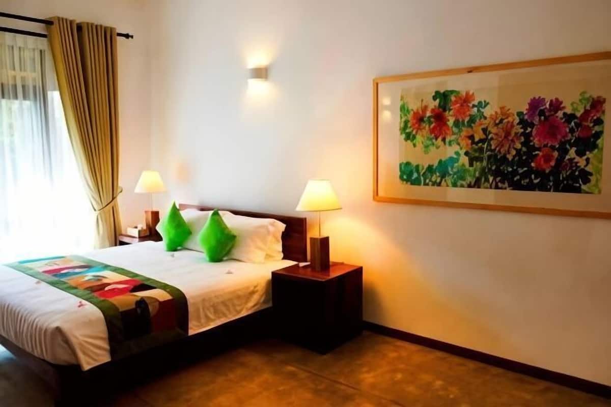 A hotel room with a bed, two bedside lamps, a painting, and a window with curtains.