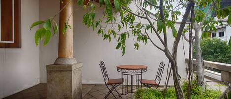 Un patio con una mesa redonda y sillas, un pilar y un árbol de hojas verdes.