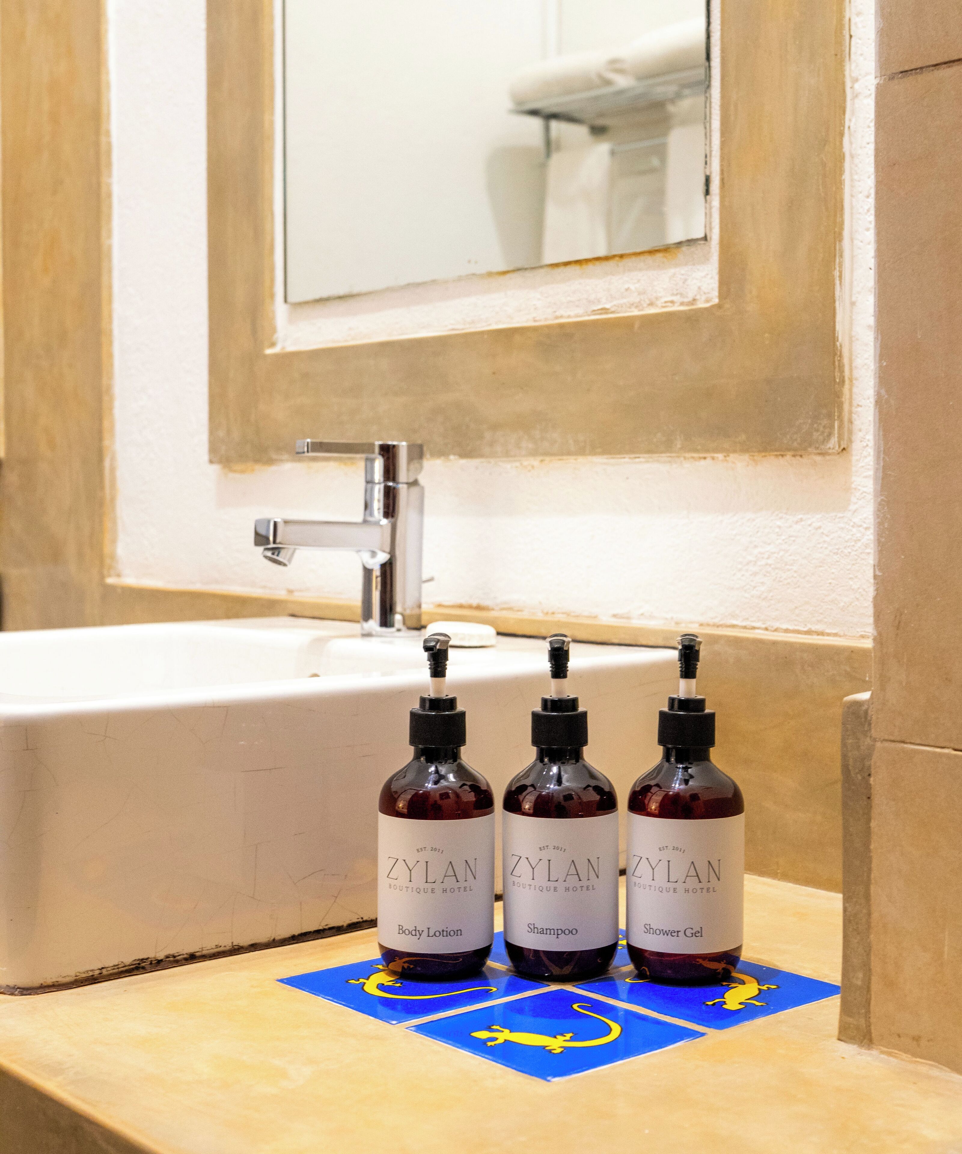 A bathroom with a sink, mirror, and three bottles of Zylan boutique hotel products on a blue mat.
