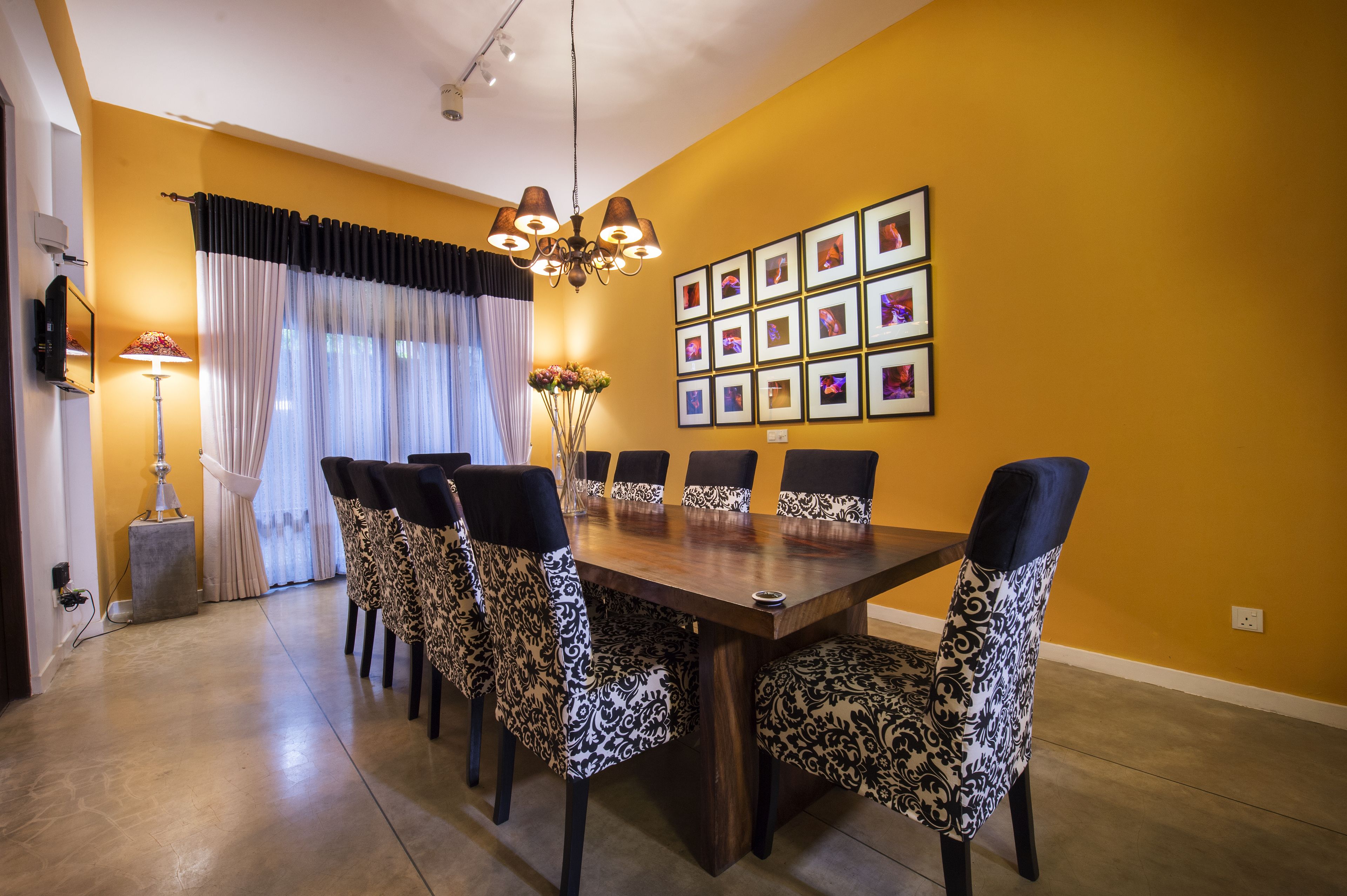A dining area with a wooden table and chairs, a chandelier, a wall of framed pictures, and a lamp.