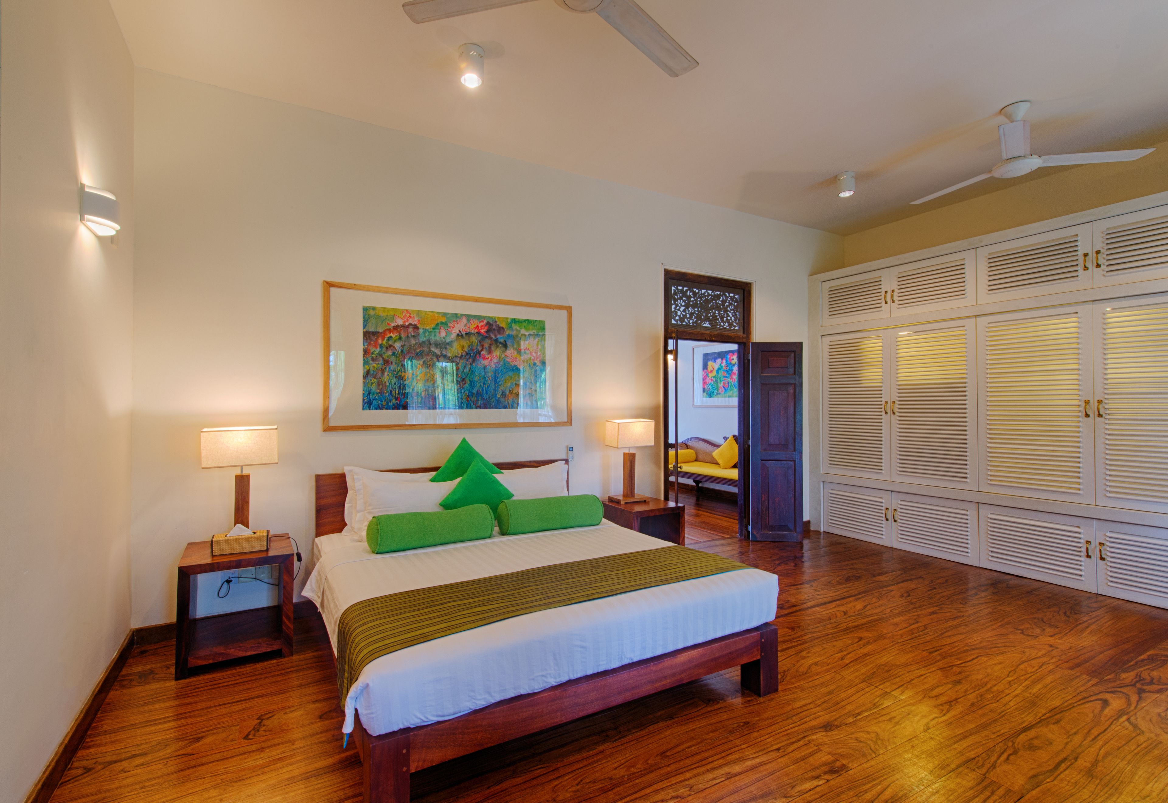 A hotel room with a large bed, two bedside tables with lamps, a ceiling fan, and a wardrobe with louvered doors.