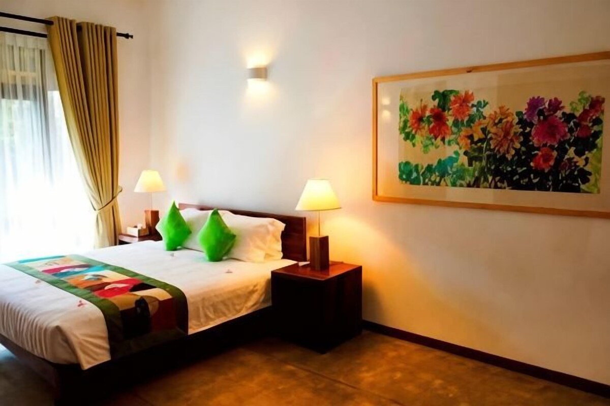 A hotel room with a bed, two bedside lamps, a painting, and a window with curtains.