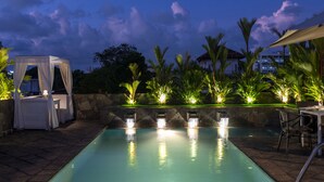 Une piscine dotée d’un auvent et d’un système d’éclairage, entourée de palmiers et d’un mur de pierre.