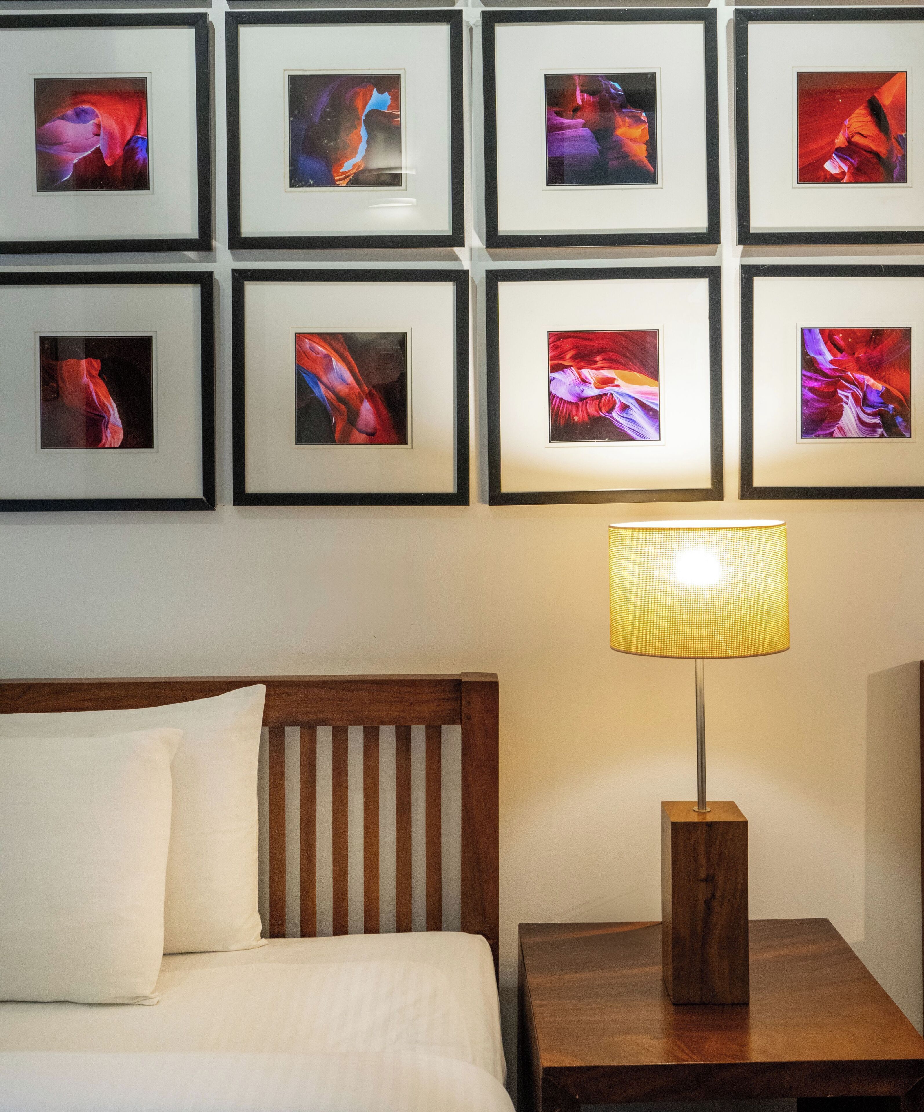 A hotel room with a bed, a nightstand with a lamp, and a wall with framed artwork.