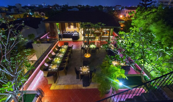 Un restaurante en la azotea con mesas al aire libre, un bar y una escalera que sube al nivel superior.