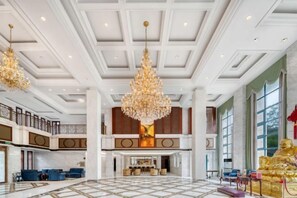 A spacious lobby with a high ceiling, chandeliers, and a grand staircase.