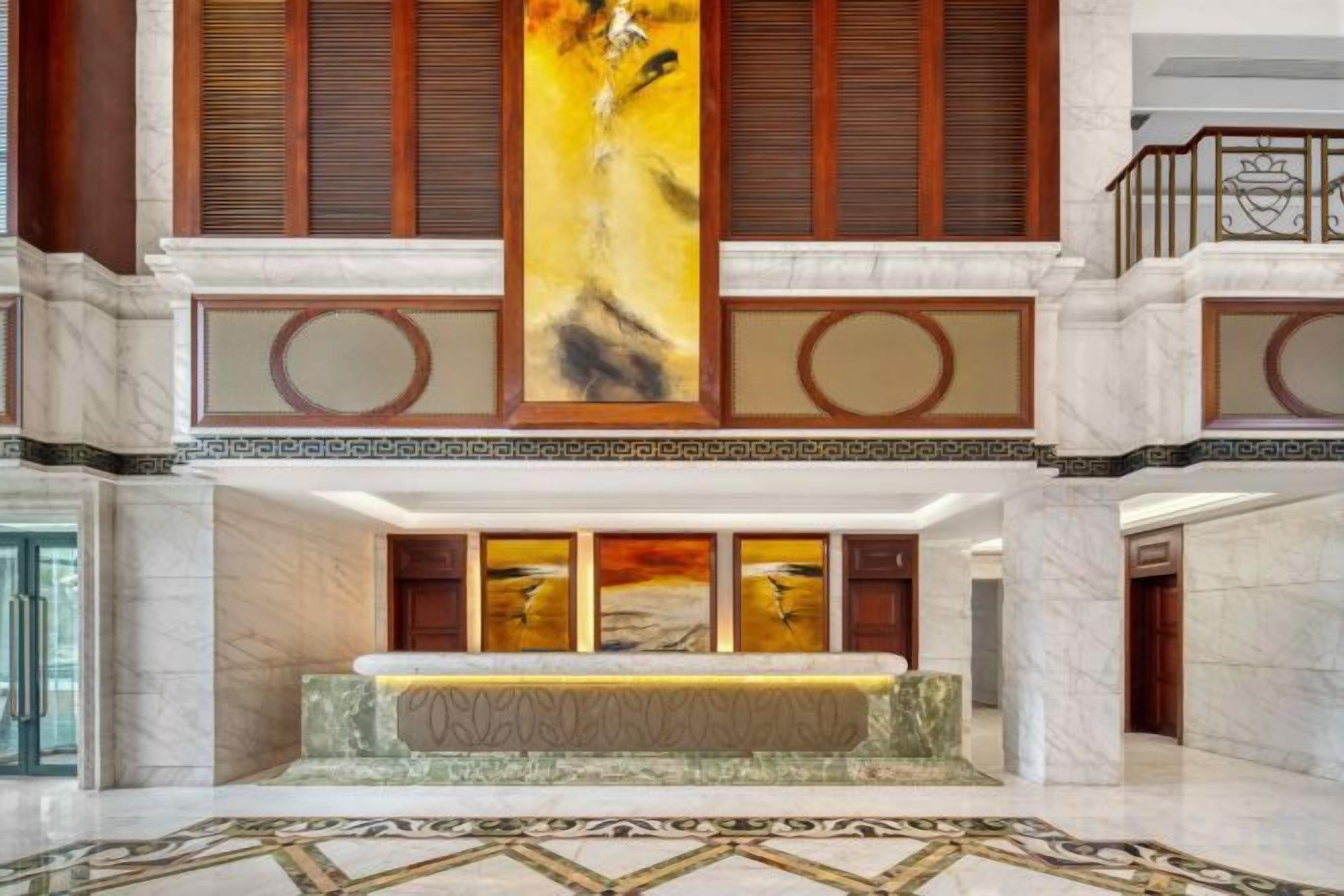 A hotel lobby with a reception desk, a large vertical artwork, and a marble floor.