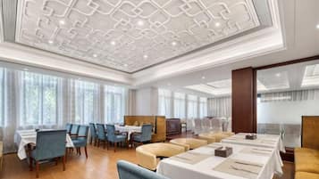 Un amplio comedor de hotel con techos altos, ventanas grandes y diversas opciones de asientos.