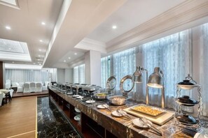 Disposição de buffet com diversos pontos de comida, bancada de mármore e área de estar com cadeiras.