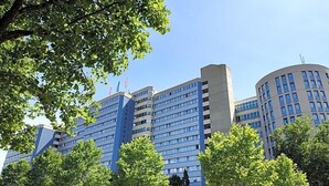 A multi-story hotel with a modern design, featuring a prominent entrance, a parking area, and a landscaped courtyard with trees. - Sommerhaus Linz (Linz)