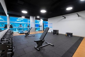 Une salle de sport équipée de matériel d’exercice, d’un banc et d’un tapis de course.