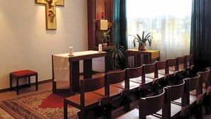 A room with a cross on the wall, a small altar, chairs arranged for seating, and a window with curtains. - Sommerhaus Linz (Linz)