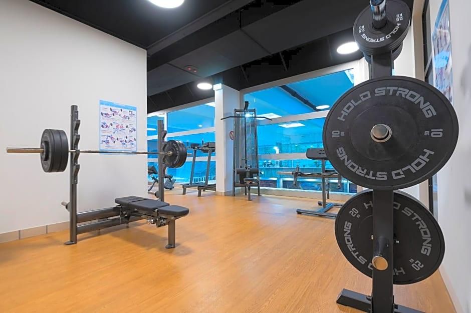 A gym with weightlifting equipment, a bench, and a mirror reflecting the interior.