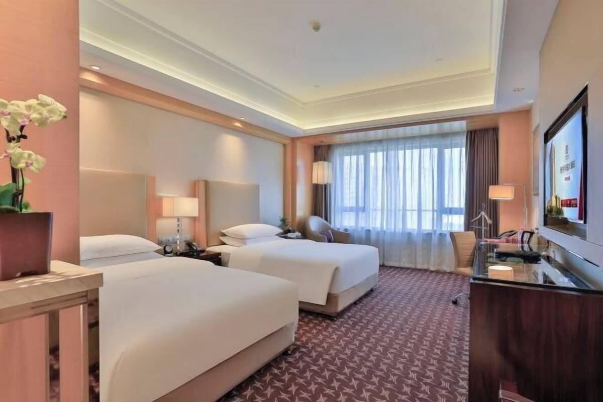 Une chambre d’hôtel avec deux lits, un bureau, une télévision et une grande fenêtre avec des rideaux.