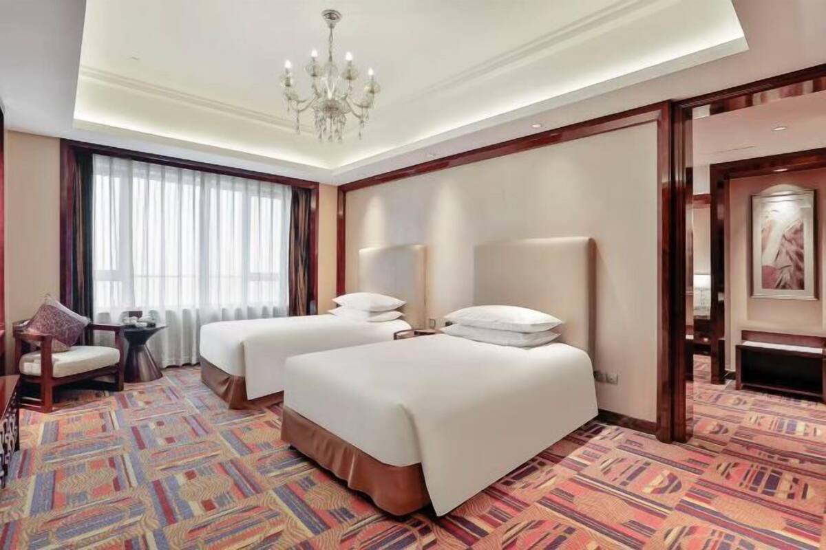 Une chambre d’hôtel avec deux lits, un lustre, une grande fenêtre avec des rideaux et une moquette à motifs.