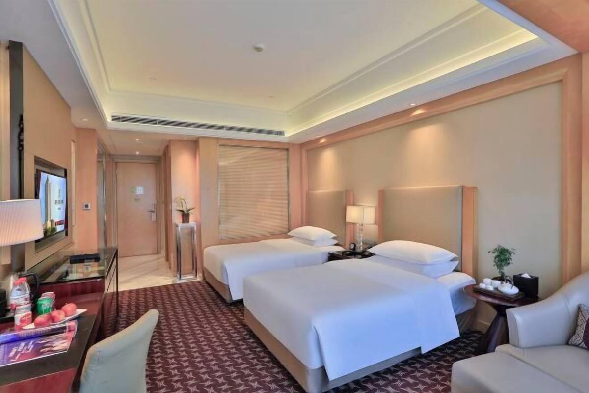 Une chambre d’hôtel avec deux lits, un bureau avec une télévision, un coin salon et une salle de bain.