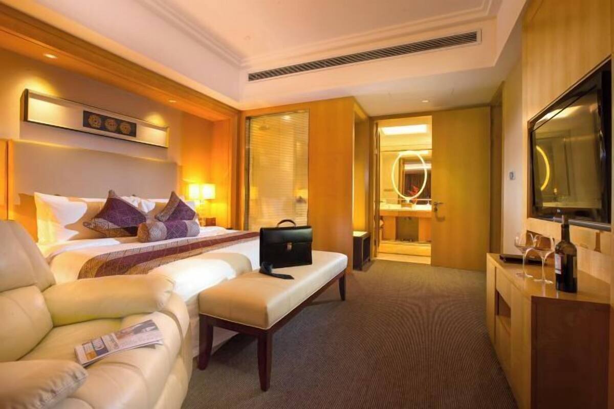 Une chambre d’hôtel avec un lit, un canapé, un bureau, une télévision et une salle de bain visible à travers une porte ouverte.