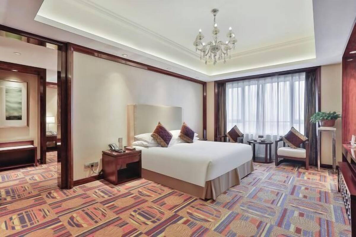 Une chambre d’hôtel avec un grand lit, un bureau, une chaise, une petite table et un lustre.